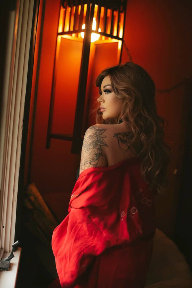 Woman in a red robe with tattoos sitting in bedroom window at Rosie O's house in Nashville.